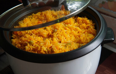 Hand lifting the lid of a rice cooker with yellow rice with tuna inside, typical Costa Rican food