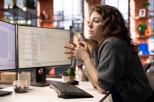 Young woman programming software code on her computer, using coding language for debugging tasks. Workspace with dual monitors helps with software engineering and web development.
