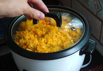 Hand lifting the lid of a rice cooker with yellow rice with tuna inside, typical Costa Rican food