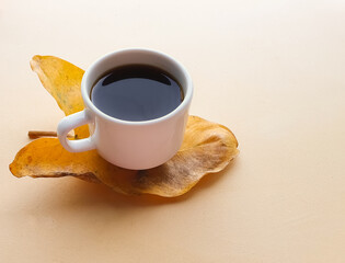 food concept of a white cup with coffee and a plate on a yellow leaf and beige background representing autumn and with space for text