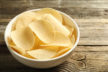 Tasty potato chips in bowl on wooden table, closeup