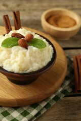 Delicious rice pudding with almonds, mint and cinnamon sticks on wooden table, closeup