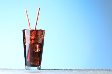 Refreshing cola with ice cubes and straws in glass on grey textured table against light blue gradient background, closeup. Space for text