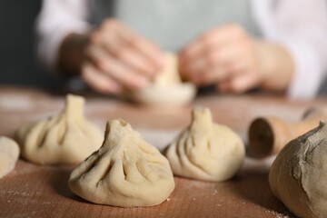 Woman making khinkali on table in kitchen, closeup