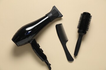 Round brush, comb and dryer on beige background, flat lay
