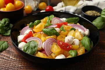 Tasty salad with yellow tomatoes, basil, onion and mozzarella cheese on wooden table, closeup