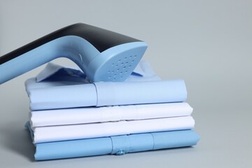 Upright steamer and stack of folded clothes on grey background, closeup