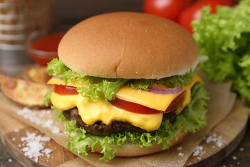 Tasty cheeseburger with potato wedges on wooden table, closeup