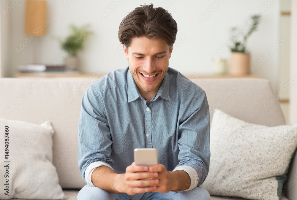 Poster mobile apps. millennial guy browsing on smatphone sitting on sofa at home.