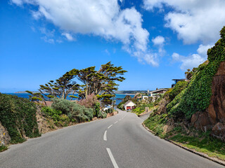 Scenic coastal road in a village. Nature, blue sea and white clouds. Le Grouet, Jersey, Channel Islands