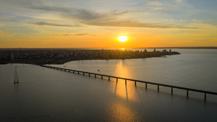 Golden hour aerial view of Posadas, Misiones, Argentina, with the Paraná River reflecting the sunset and part of the San Roque González bridge visible on the right.