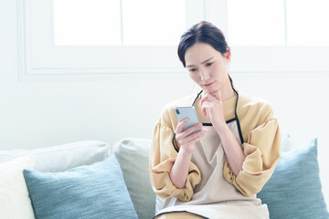 困った表情でスマートフォンを使うエプロンをつけた主婦