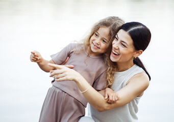 Obraz premium A young mother and her five-year-old daughter are standing on the pier by the lake and looking at the water.