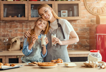 Happy mother and daughter drinking milk and bonding at kitchen, cooking together, copy space