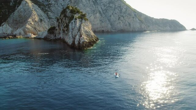 Person kayaking in a calm bay near dramatic limestone cliffs on Kefalonia island in Greece