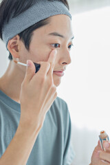 目元にコンシーラーを塗る若い男性