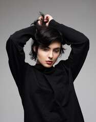Stylish young woman with short haircut in black sweater posing on gray background.