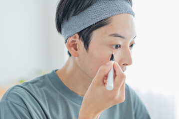 目元にコンシーラーを塗る若い男性