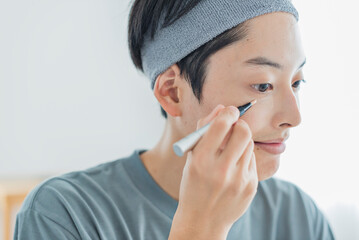 目元にコンシーラーを塗る若い男性