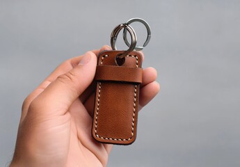 Hand holding a simple brown leather keychain with stitching detail against a plain neutral background
