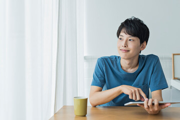 休日にタブレット端末で動画を見る若い男性