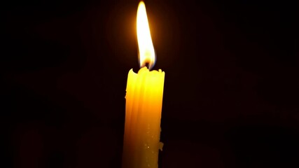 Illuminated yellow wax candle with a bright flame glowing in the dark for holiday celebrations or commemorating a solemn occasion