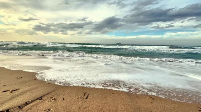 Experience the tranquility of serene beach waves gently rolling in beneath a dramatic and cloudy sky overhead