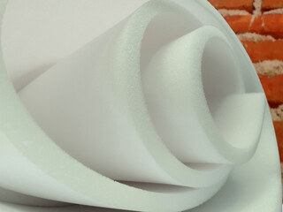 a roll of thin white sponge foam material in a room with red brick walls