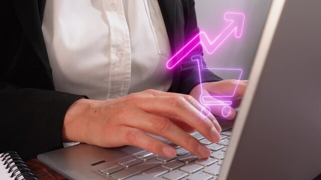 Businesswoman working on her laptop, with a hologram of a shopping cart icon with an upward arrow. Concept of increased sales. - Powered by Adobe