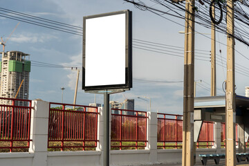 Vertical blank billboard with copy space on city street near power pole and red fence under clear...