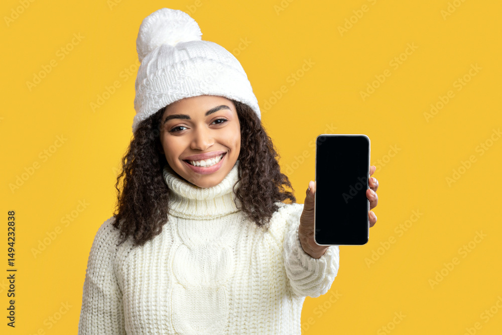 Poster modern technology concept. smiling african american woman in winter hat holding cellphone with empty