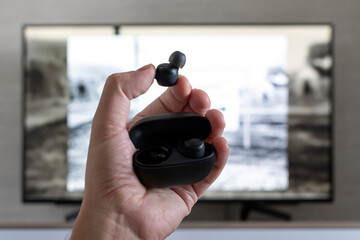 wireless headphones in the hands of a man on background of a TV screen. watching TV with headphones at night.