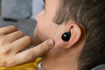 Close-up of wireless earphone in human ear on dark background. insert earphone into the ear
