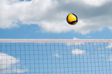 volleyball ball flies over the net against a blue cloudy sky. Beach volleyball