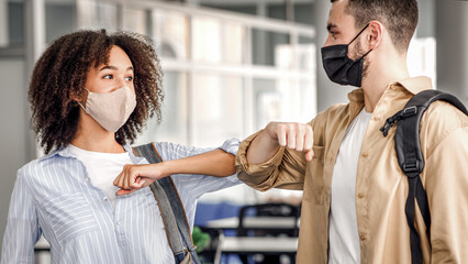 Touching elbows to say hello and social distance during covid-19 pandemic. Young man and african american woman greeting at work in morning in coworking office interior, empty space