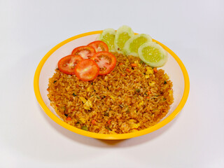 A vibrant plate of Nasi Goreng, or Indonesian fried rice, rests on a bright white surface. The reddish-brown rice is generously garnished with vibrant red tomato slices and crisp green cucumber