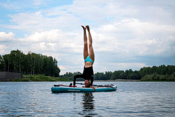 Woman practicing SUP yoga, on a paddleboard against background of nature. sporty girl on a board in...