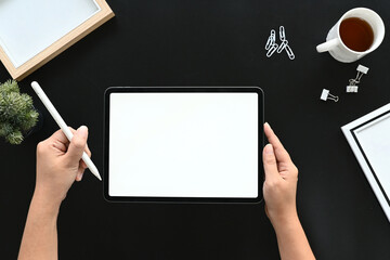 Top view office desk with hands holding tablet while working in dark modern workplace, empty screen tablet for your present.