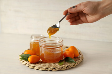 Kumquat fruits, jars with jam  and spoon in hand on light background