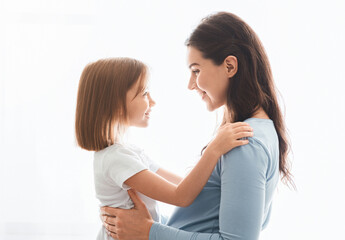 Lovely pregnant mother and little daughter cuddling over white background, family portrait
