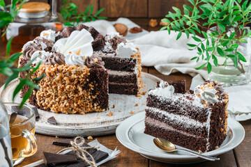 Chocolate biscuit cake with cream, nuts on wooden background with flowers and nuts. Holiday dessert, sweets and pastry, close up