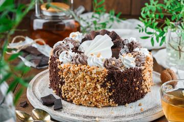 Chocolate biscuit cake with cream, nuts on wooden background with flowers and nuts. Holiday dessert, sweets and pastry, close up
