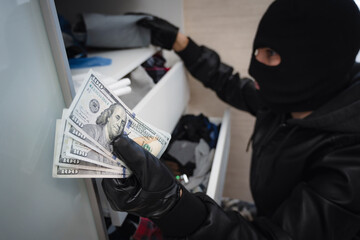 thief in a black mask searches a closet with clothes in search of cash or valuables. Apartment...