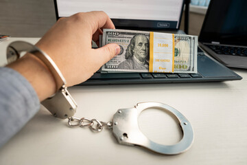 Handcuffs and dollar banknotes on laptop keyboard. Online crime concept.