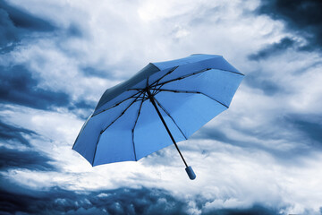 Blue umbrella flying in cloudy sky. Stormy weather
