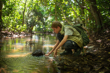 Young boy crouches at the edge forest stream connection between a  learning from the environment holiday ecotourism concept.