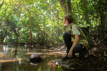 Young boy crouches at the edge forest stream connection between a  learning from the environment holiday ecotourism concept.