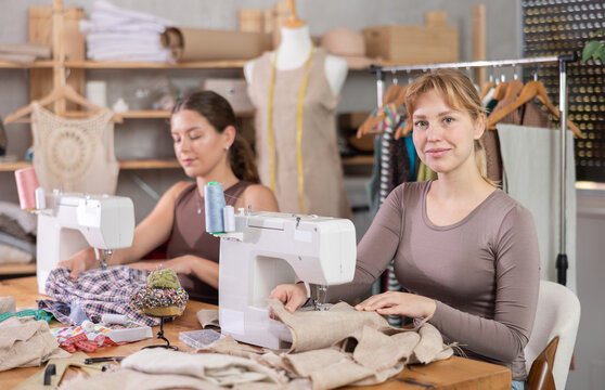 Two dedicated young female fashion designers sewing custom garments at machines, focusing on precision and detail, bringing creative visions to life in collaborative studio filled with inspiration..