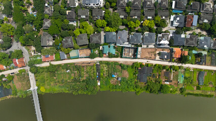 Top-down drone view of a narrow canal bordered by lush greenery and adjacent residential villas with gardens, illustrating Vietnam’s blend of waterways and suburban housing.