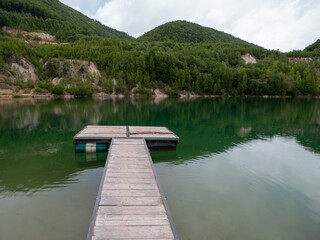 Floating wooden pier on a clear green lake in a flooded quarry surrounded by forested hills and...